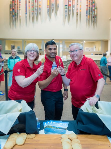 Three staff in red Salvation Army shirts smiling behind a registration table
