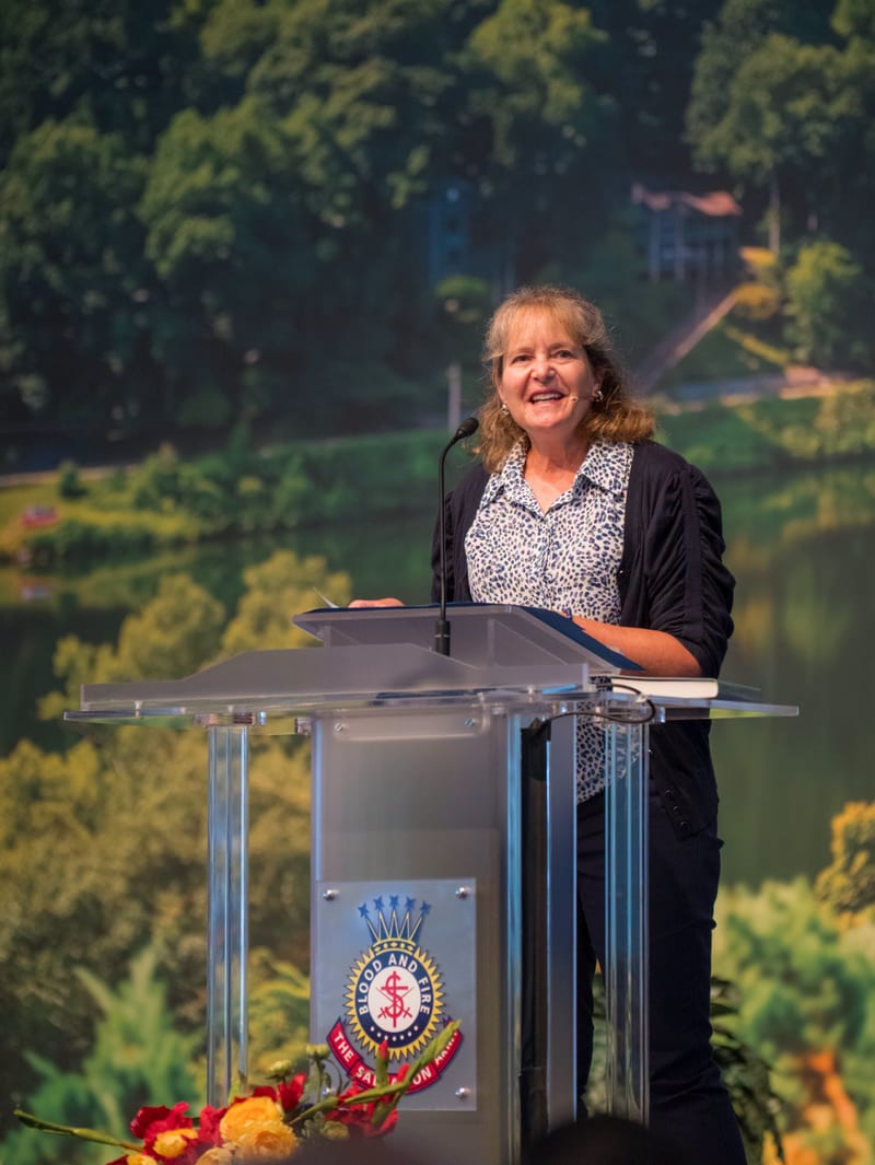 Dr. Ellen Marmon speaking from a lectern bearing the Salvation Army crest