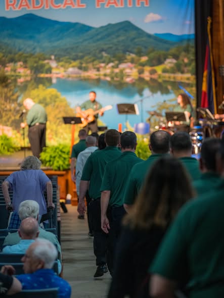 Men in matching green shirts filing toward the stage beneath a Radical Faith lake banner