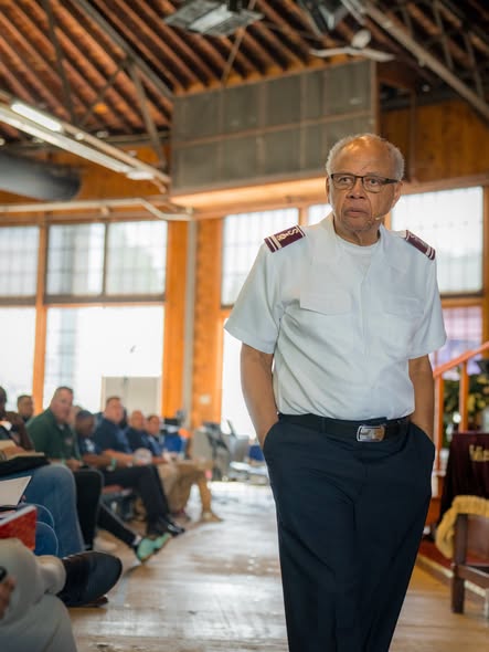 Commissioner Israel Gaither walking as he speaks in a timber-beamed hall