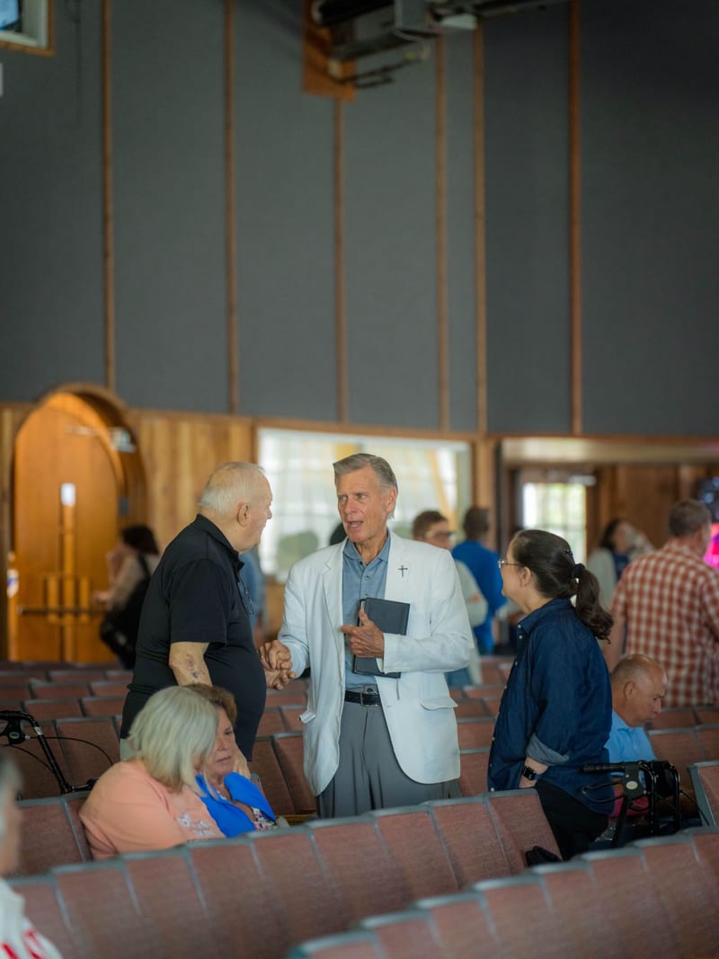 A man in a white jacket holding a Bible in conversation with others between the pews