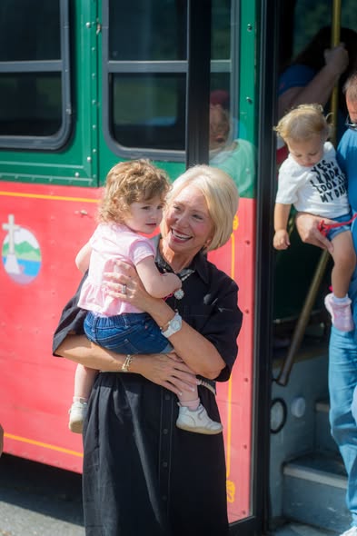 A woman holding a toddler beside the conference trolley as another child is lifted aboard